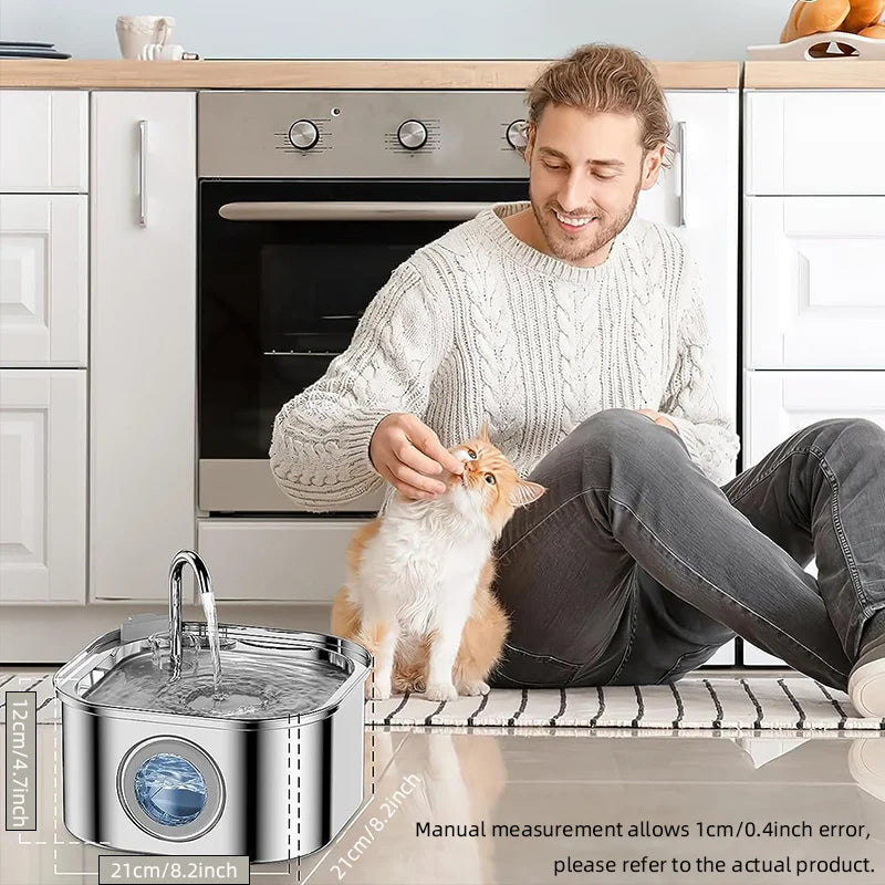 Man sitting on a kitchen floor with a cat next to a pet water fountain.